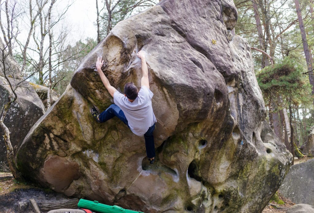climber ascending boulder in the forest