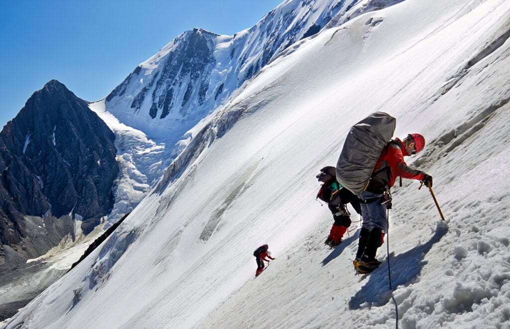 Team of alpinists on a snowy mountain. The first one climbs with a piolet.