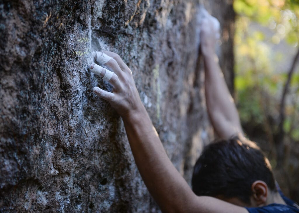 Climber climbing boulder with tape directly on the fingers to avoid being hurt