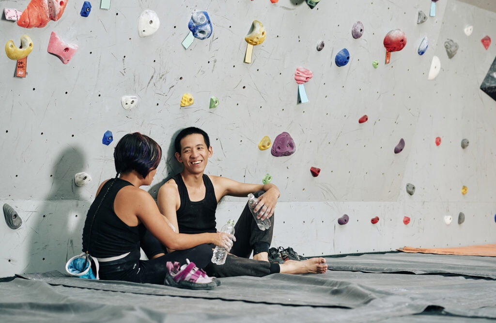 Cheerful young man and woman drinking fresh water and talking when resting after climbing at bouldering center