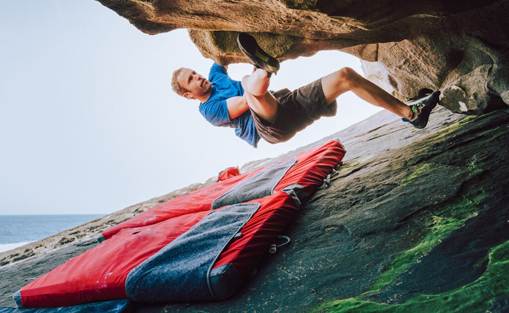 Young boulder climber man climbing with safety mats