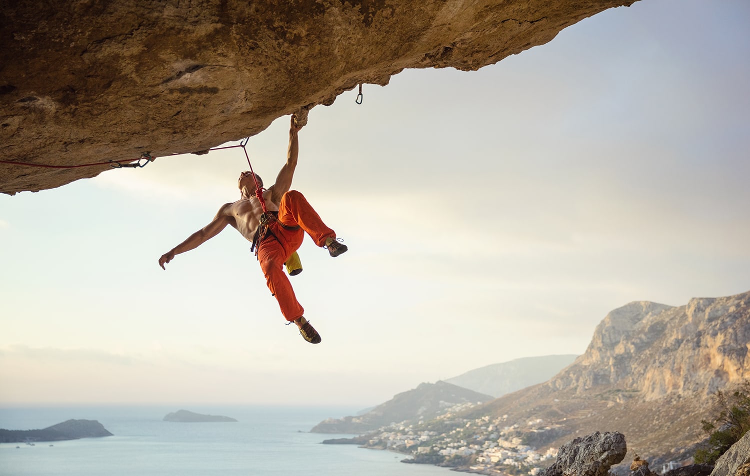 Young man climbing challenging route in cave against beautiful view of coast