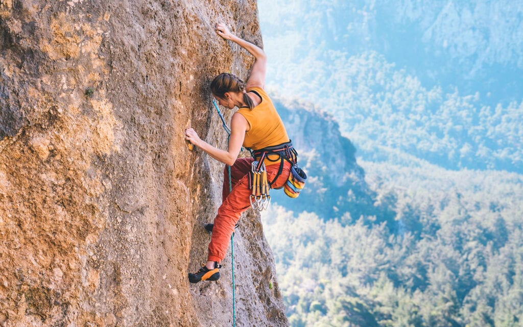 Young athletic woman climbs an overhanging rock with rope 