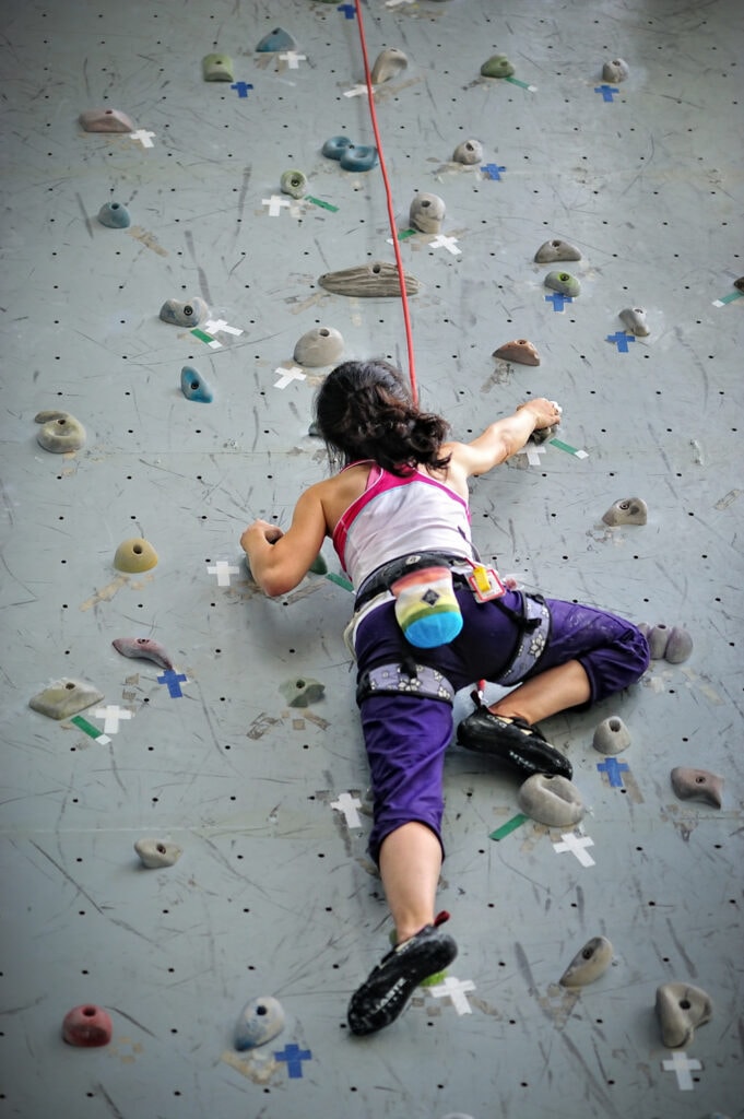 Asian girl wearing harness and belaying rope, climbing on a very high rock climbing wall