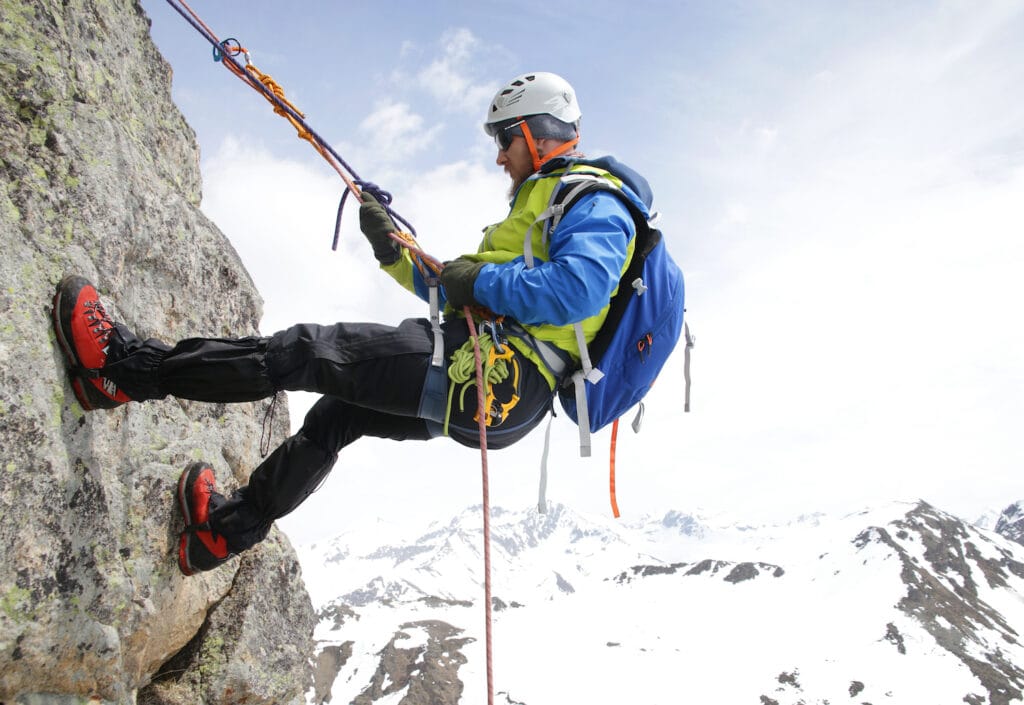 Mountaineer rappelling off a high cliff with a prusik on the main rope as fall protection for a secure descent