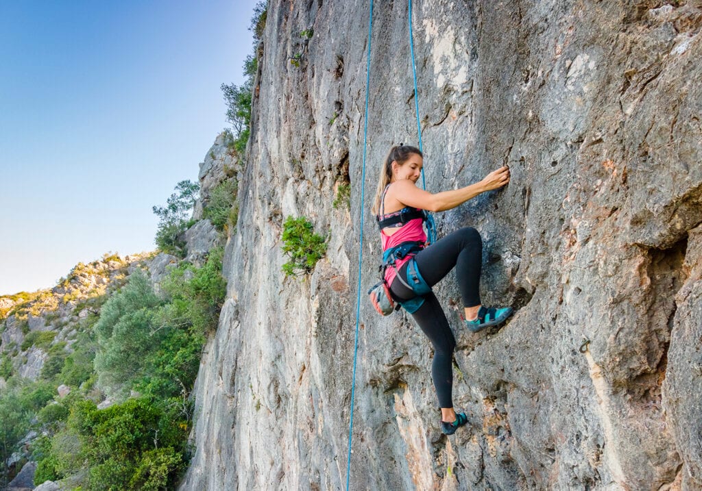 A woman in harness climbing a steep rock in Portugal