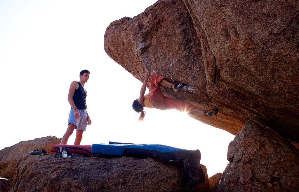woman bouldering with a friend spotting her for safety