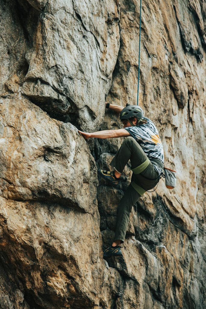 man rock climbing on brown rock wearing rock climbing harness