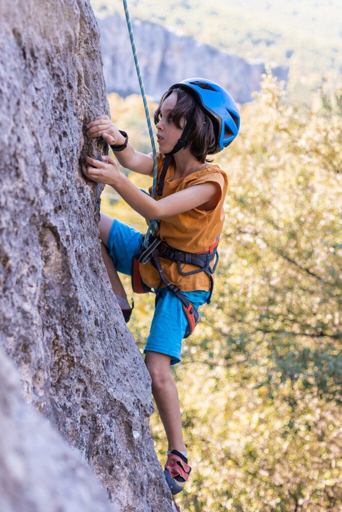 child rock climbing wearing harness and helmet for safety