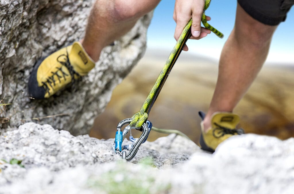 Climber reaches the summit of a mountain and uses auto-locking carabiners to build an anchor