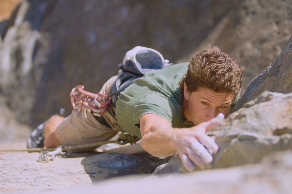 climber wearing technical clothing with harness and shoes lead climbing a pitch