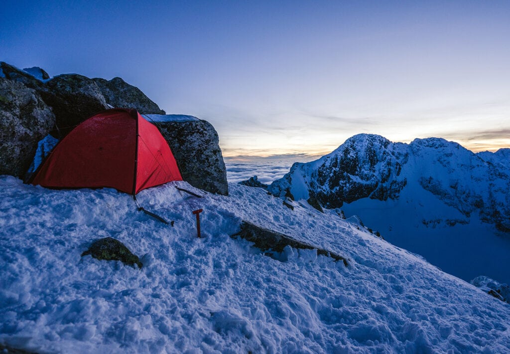 red tent next to rocks on the snow in nature