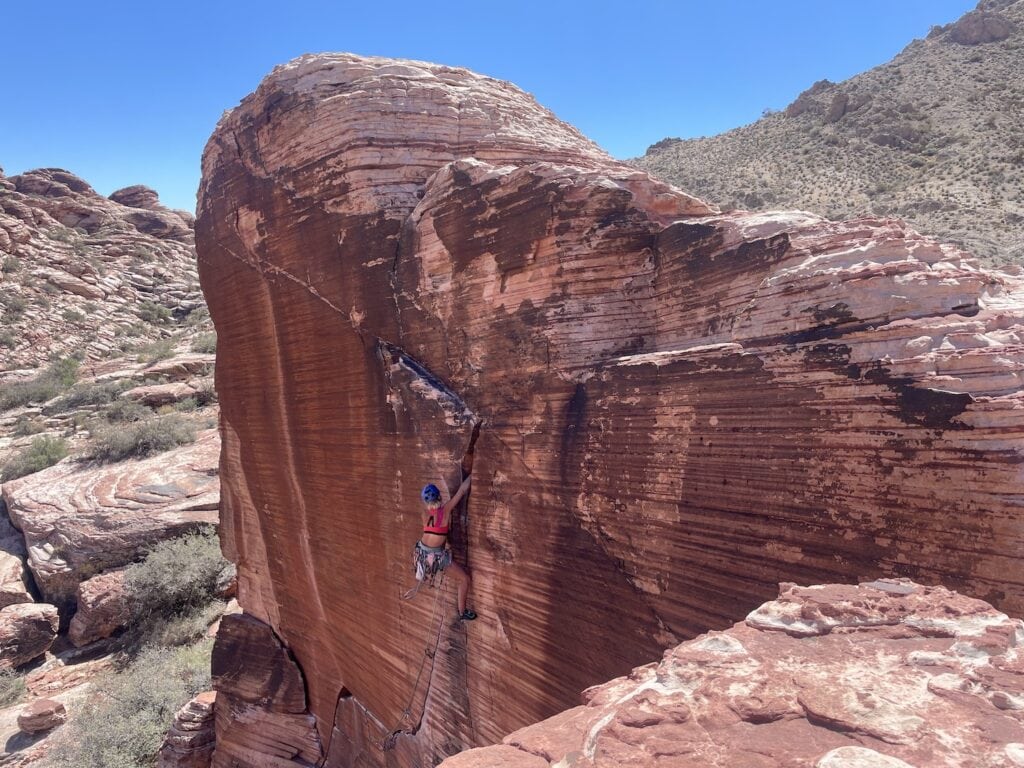 Wren (writer climber) in Red Rocks where she's pushing outwards to ascend a difficult climb