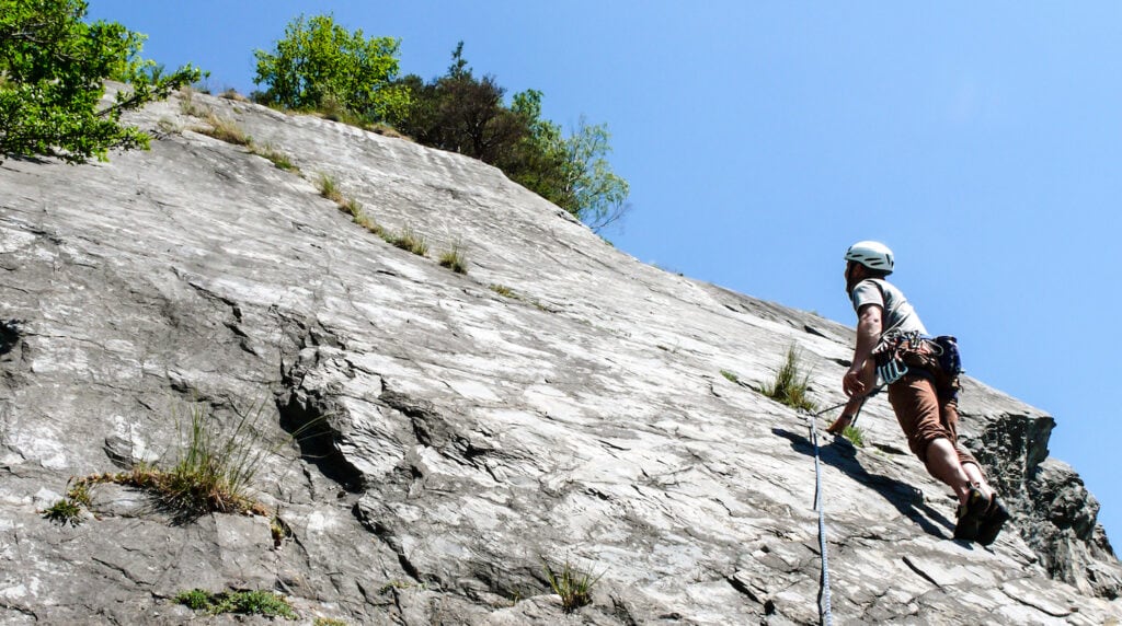 climber progressing on tiny edges on a slab rock face (bolts are visible above the knees)